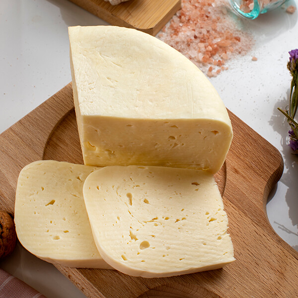 Um pedaço de queijo amarelo claro com duas fatias em uma tábua de cortar de madeira